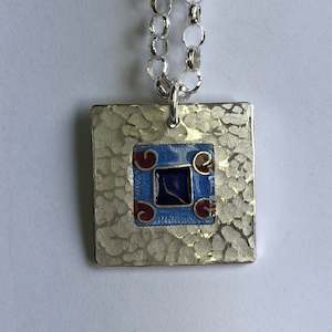 Pendant: Pendant, blue on blue square with 4 red koru's
